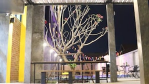 An outdoor covered area with a tree, concrete pillars, and a tiled floor.