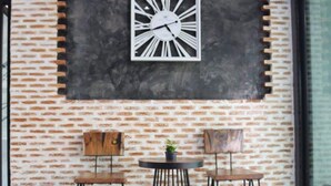 A patio area with a brick wall, a clock, two chairs, and a small table.