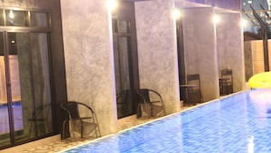 A pool area with tiled flooring, chairs, and a yellow umbrella.