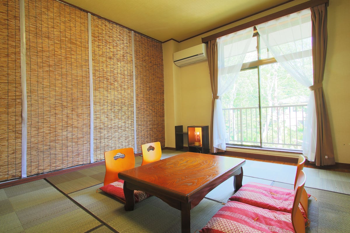 Una habitación japonesa tradicional con suelo de tatami, una mesa de madera baja y sillas naranjas.