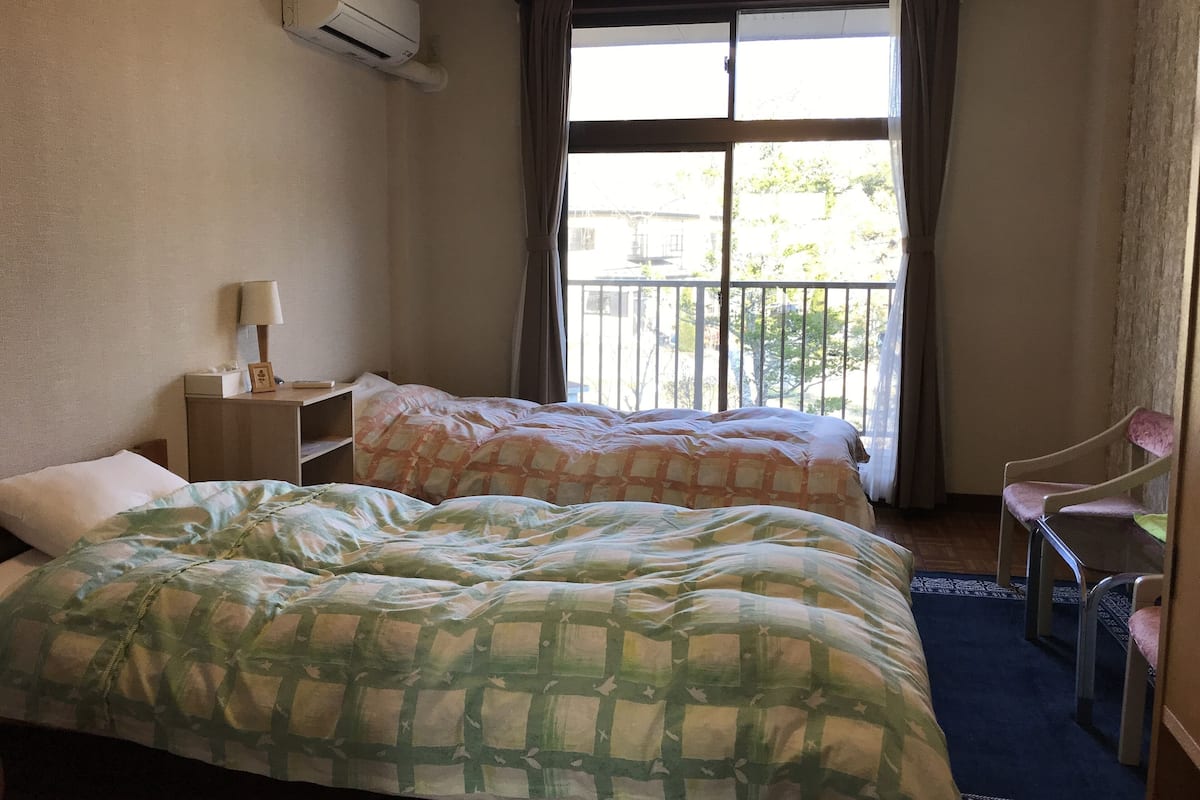 Habitación de hotel con dos camas, un escritorio, una silla y un balcón con vistas.