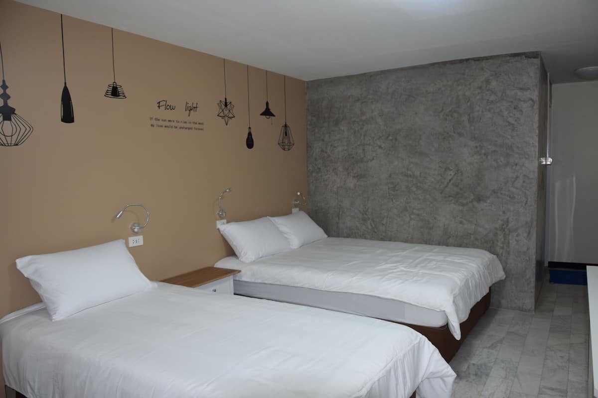 A hotel room with two single beds, a large window, and a textured gray wall.