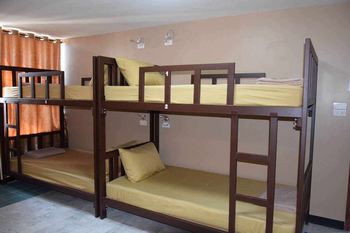A bunk bed room with two levels, each with a mattress and pillows.