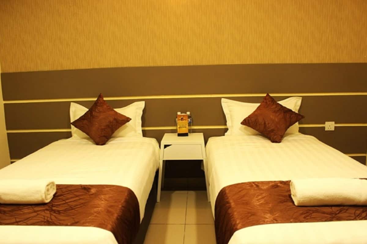 A hotel room with two single beds, each with a brown headboard, white bedding, and a small bedside table with a bottle.