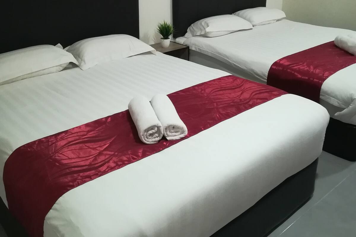 A hotel room with two beds, each with white linens and red bedspreads. There is a small potted plant on the nightstand between the beds.