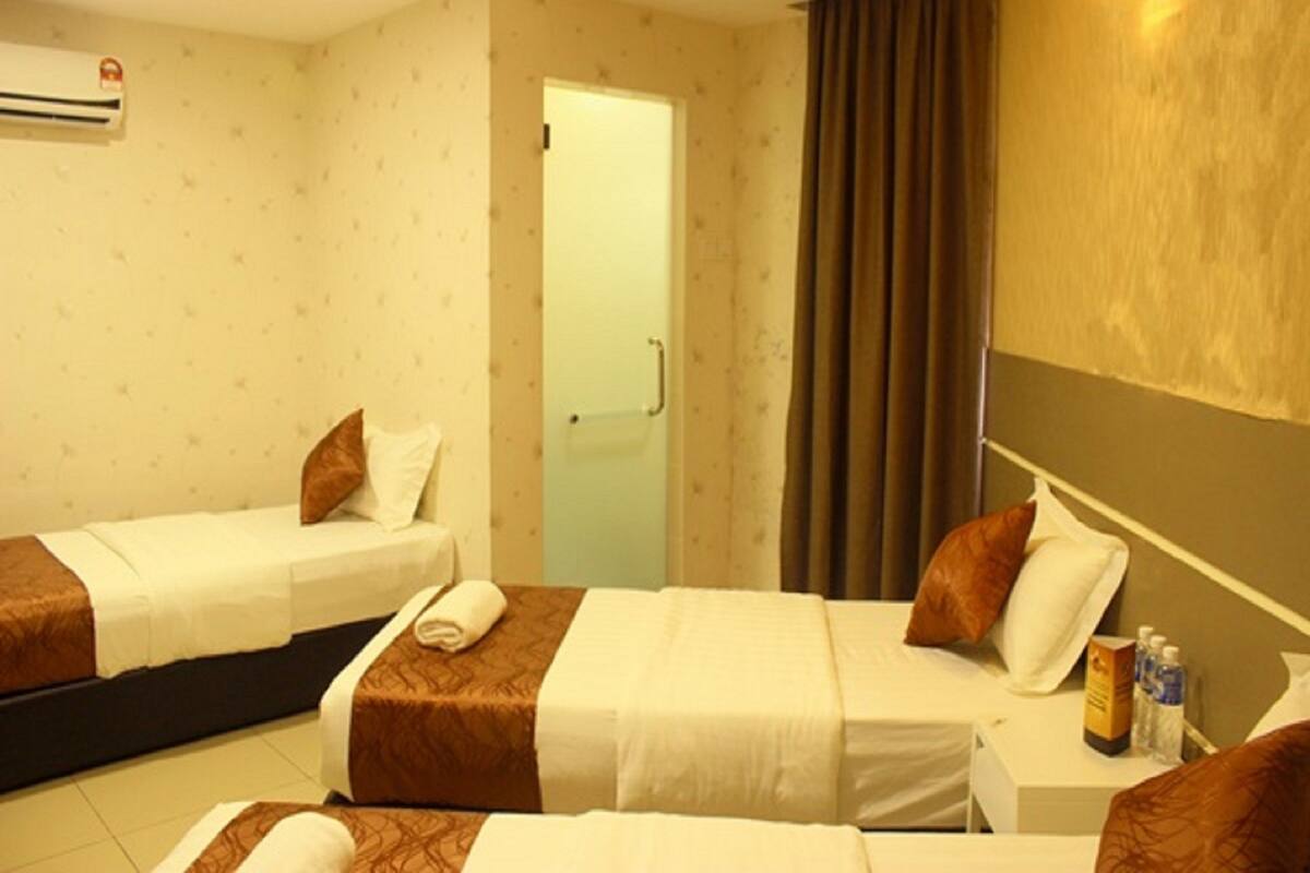 A hotel room with two single beds, a small table with a bottle, and a door leading to another room.