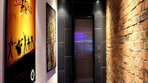 A hallway with a brick wall, an elevator, and a poster of a rock band on the wall. - Rock & Roll Hotel (Klang)