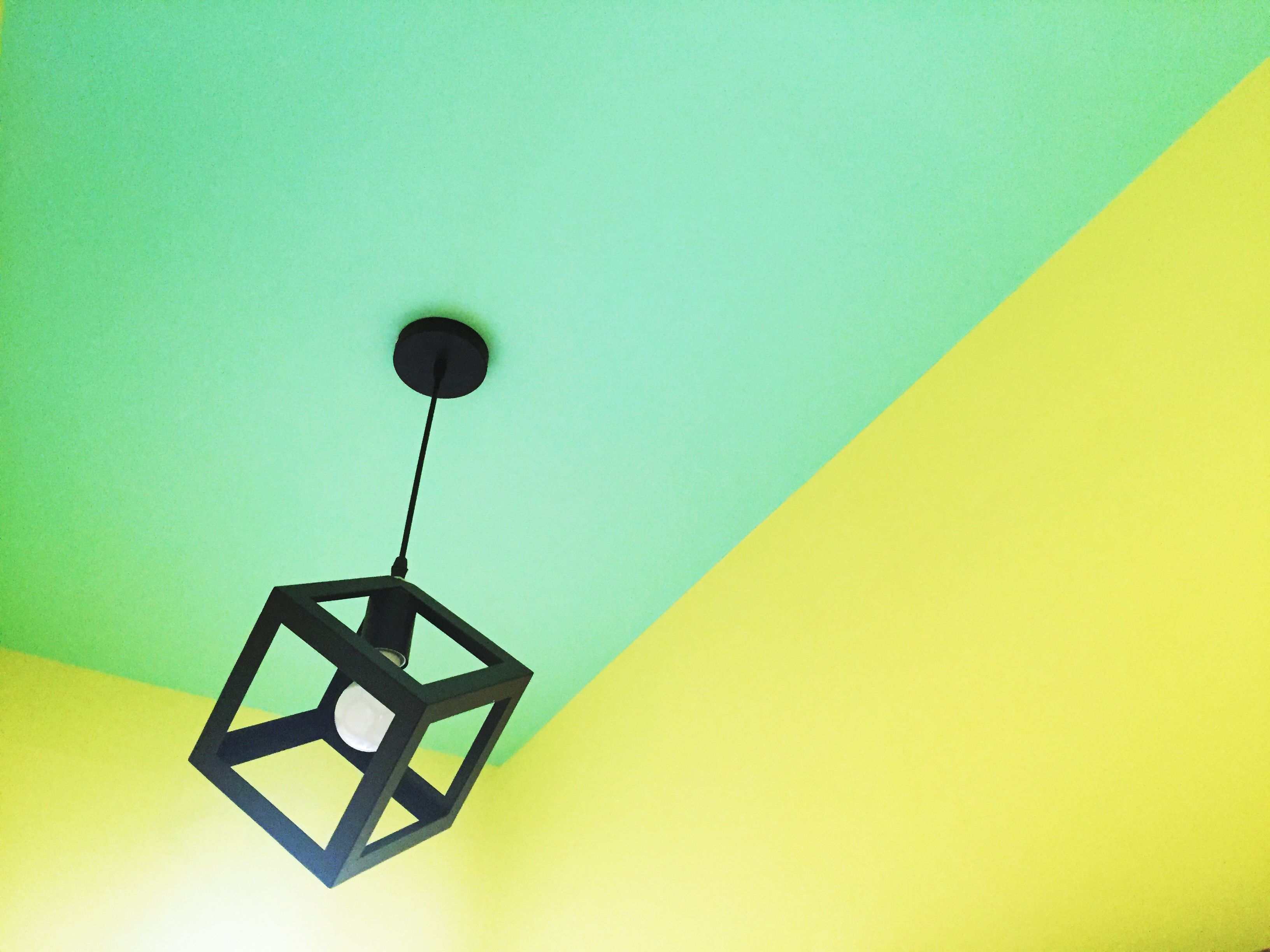 Un luminaire suspendu de forme géométrique, doté d’une ampoule blanche, fixé à un support noir au plafond.