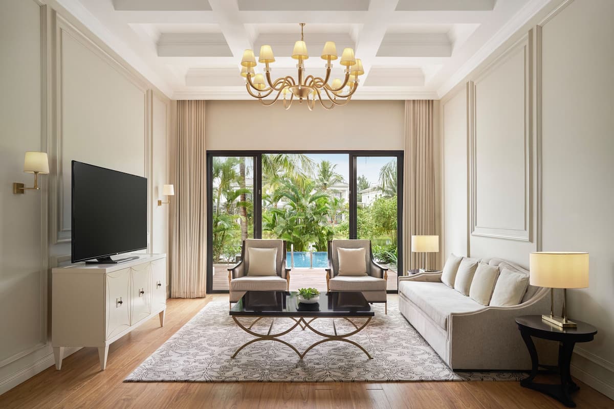 A modern living room with a TV, two armchairs, a sofa, a coffee table, and a chandelier.