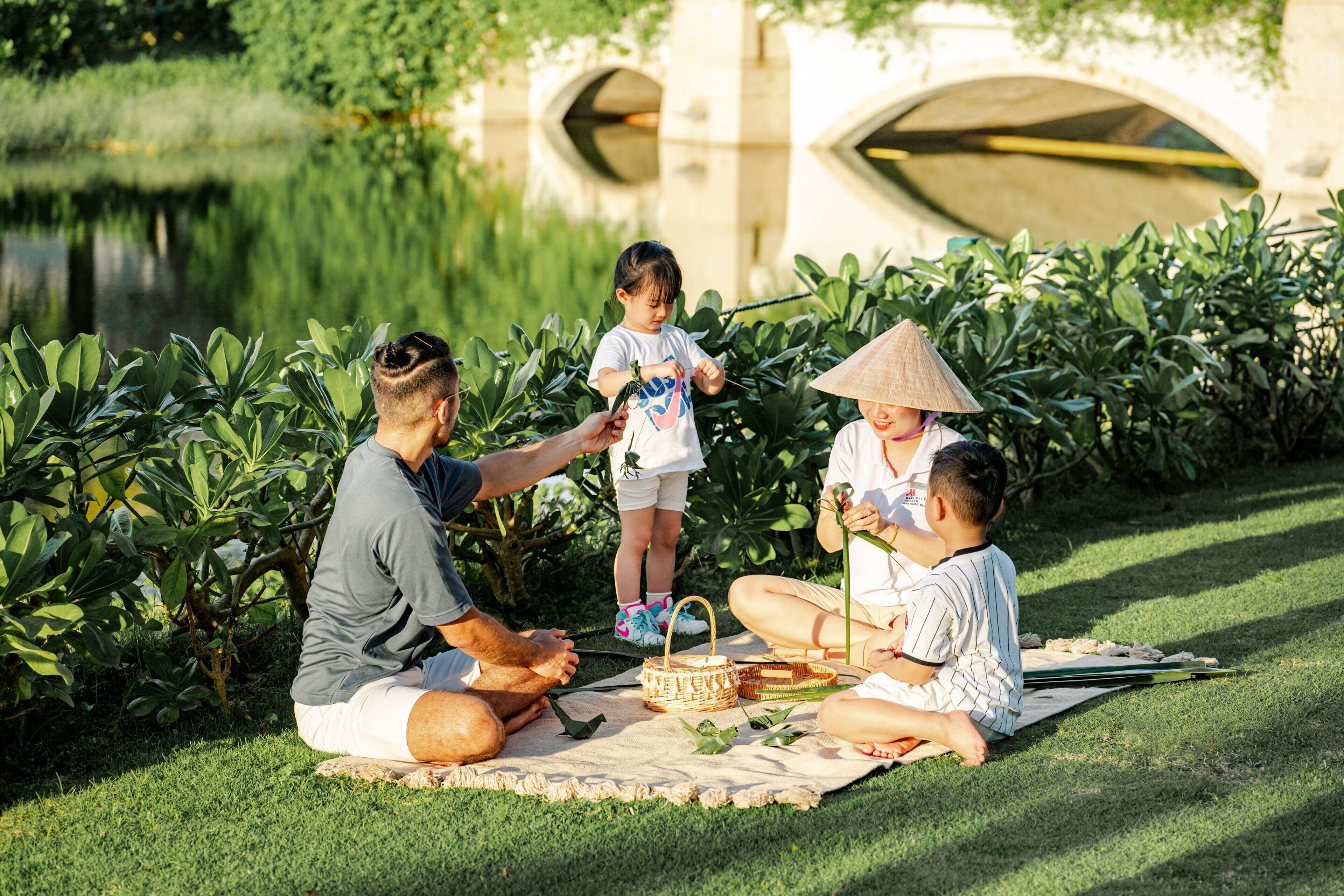 Un pique-nique en famille sur une pelouse, avec un pont de pierre en arrière-plan.