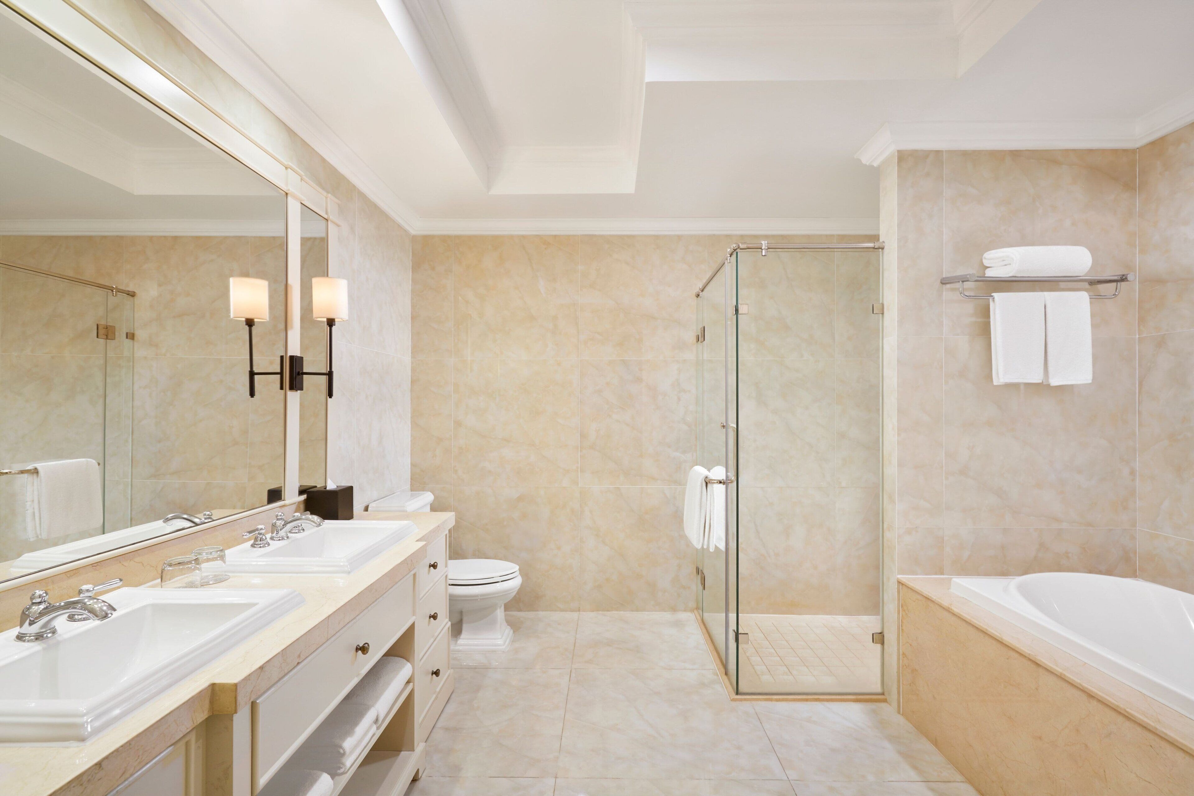 Een moderne badkamer met twee wastafels, een toilet, een douche met glazen wand en een bad.