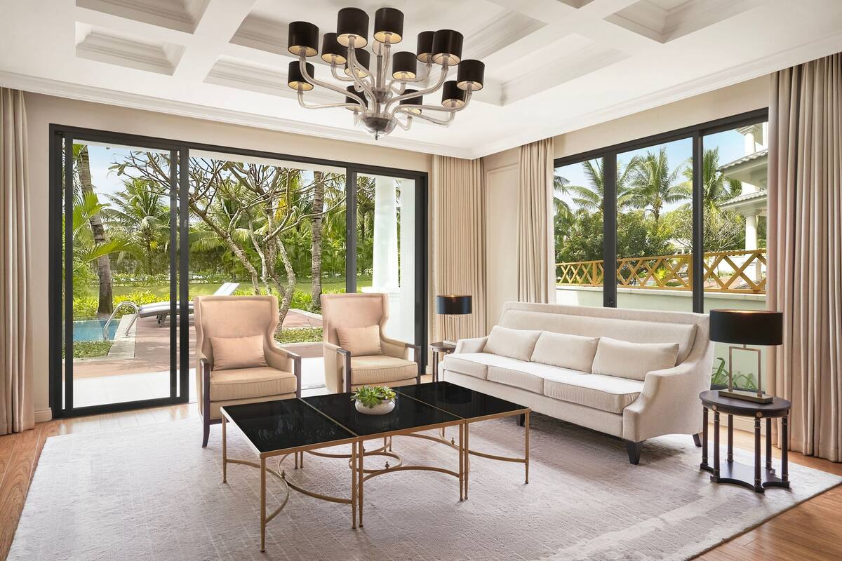 A spacious living room with a large window, a black coffee table, a beige sofa, and a chandelier.