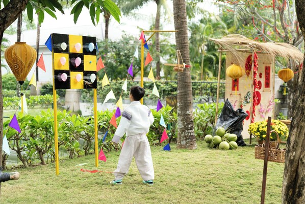 A child playing a game with colorful flags and a checkered board in a garden with palm trees and a small structure. - Danang Marriott Resort & Spa, Non Nuoc Beach Villas (Da Nang)