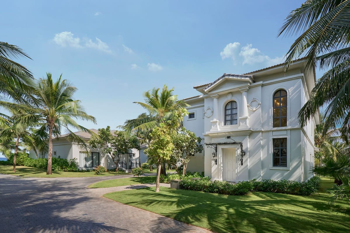 A white colonial-style building with arched windows and a central door, surrounded by well-maintained lawns and palm trees.