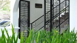Un edificio blanco con una reja metálica negra y una escalera que conduce a un nivel superior.