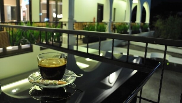 Una taza de café sobre una mesa, con vista a un edificio con arcos y barandilla de balcón.