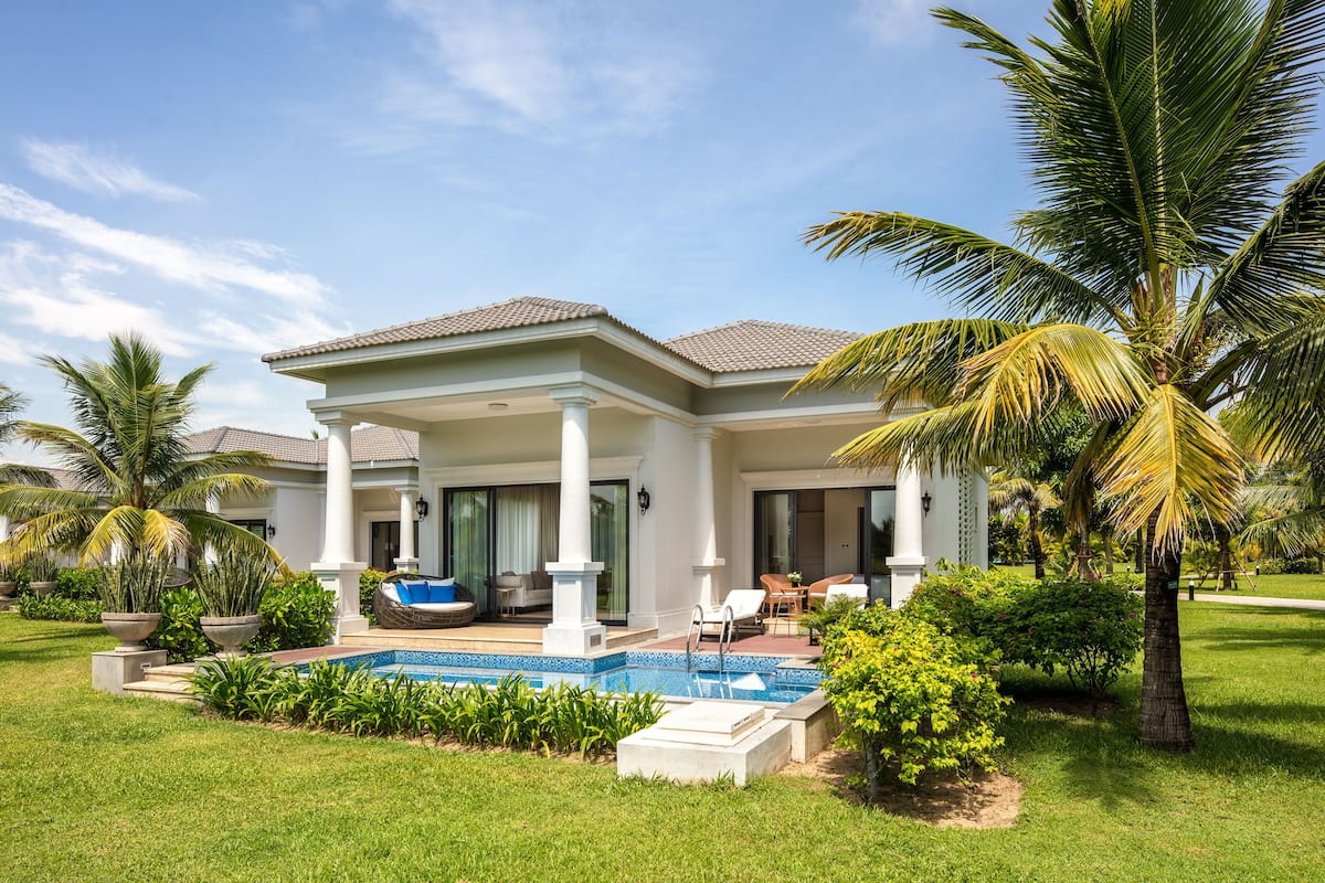 A two-story house with a swimming pool, palm trees, and a well-maintained lawn.