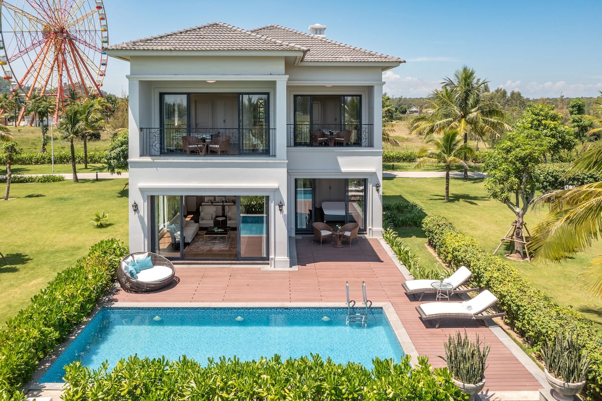 A two-story house with a swimming pool, outdoor seating, and a Ferris wheel in the background.