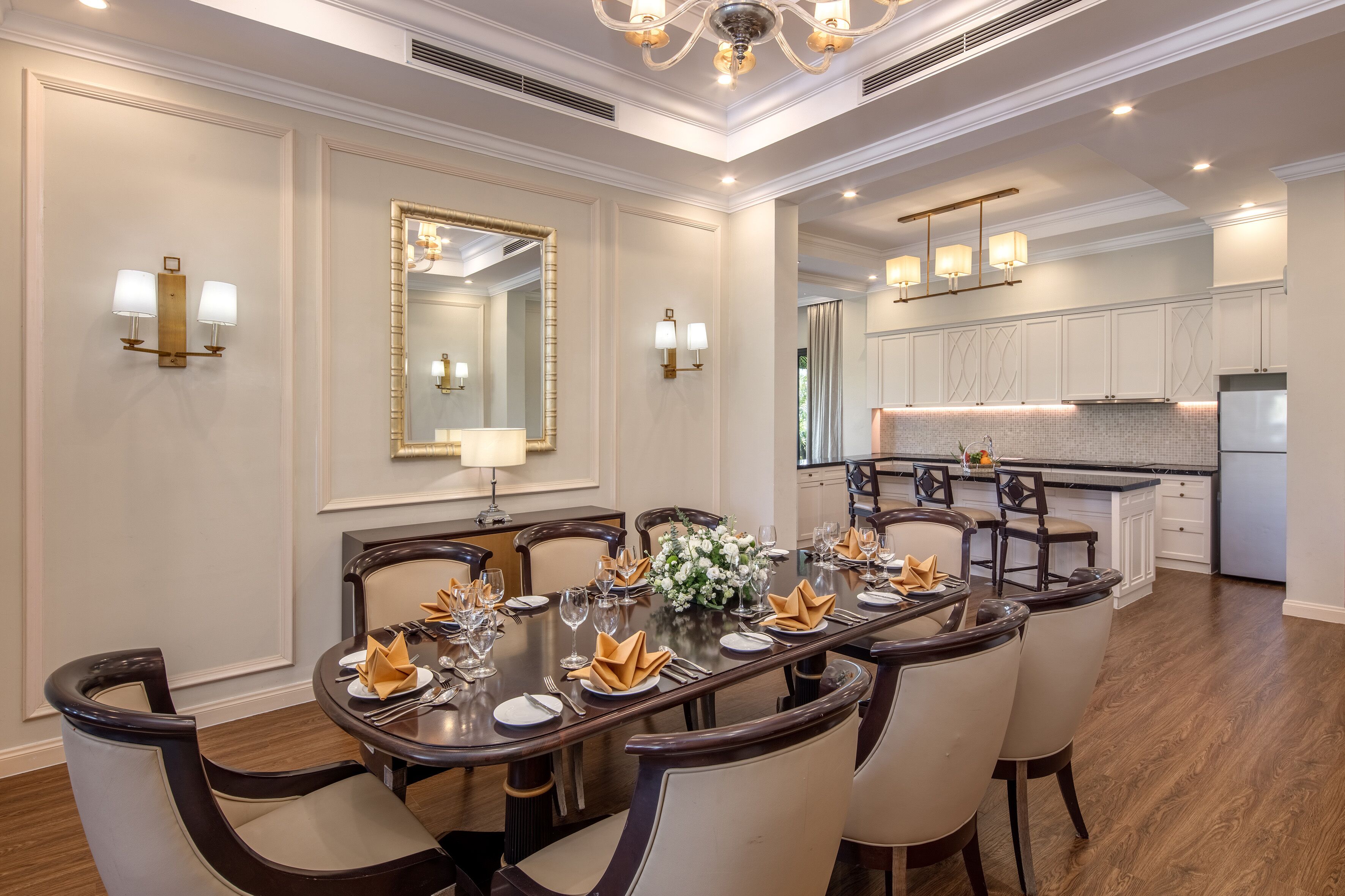 A formal dining room with a long table set for six, flanked by two wall sconces and a large mirror.