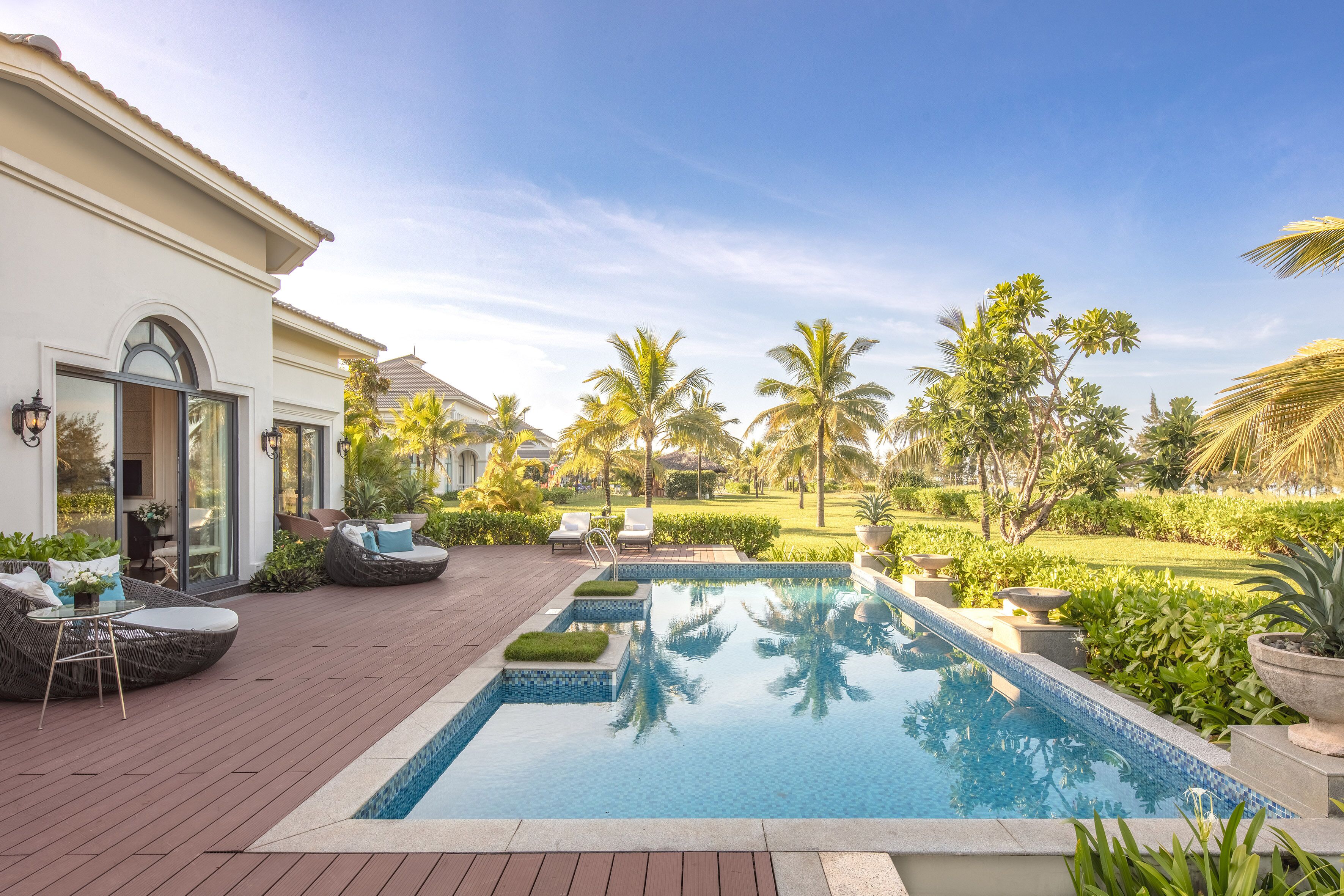 A pool area with lounge chairs, a wooden deck, and a landscaped garden with palm trees.