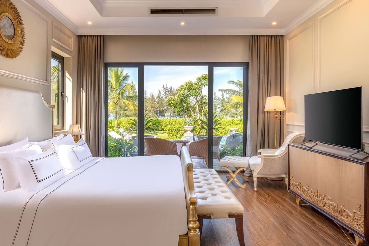 A hotel room with a large bed, a television, a sofa, and a view of the outdoors.