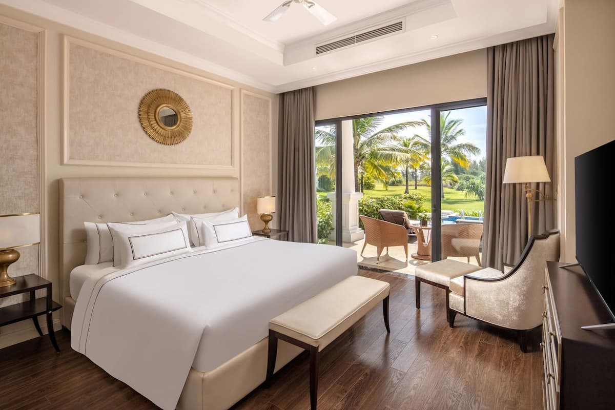 A hotel room with a large bed, a desk, a chair, a TV, and a view of a pool and palm trees.