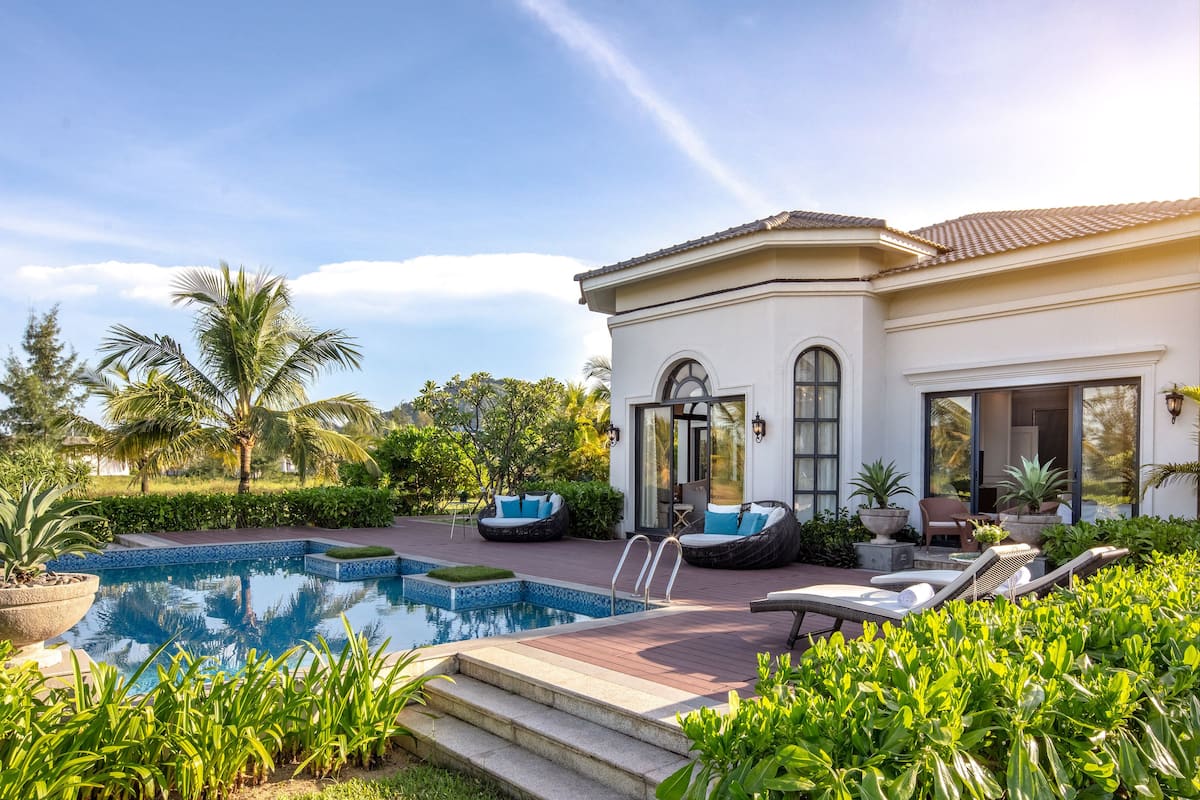 A pool area with a white building, palm trees, and outdoor seating.