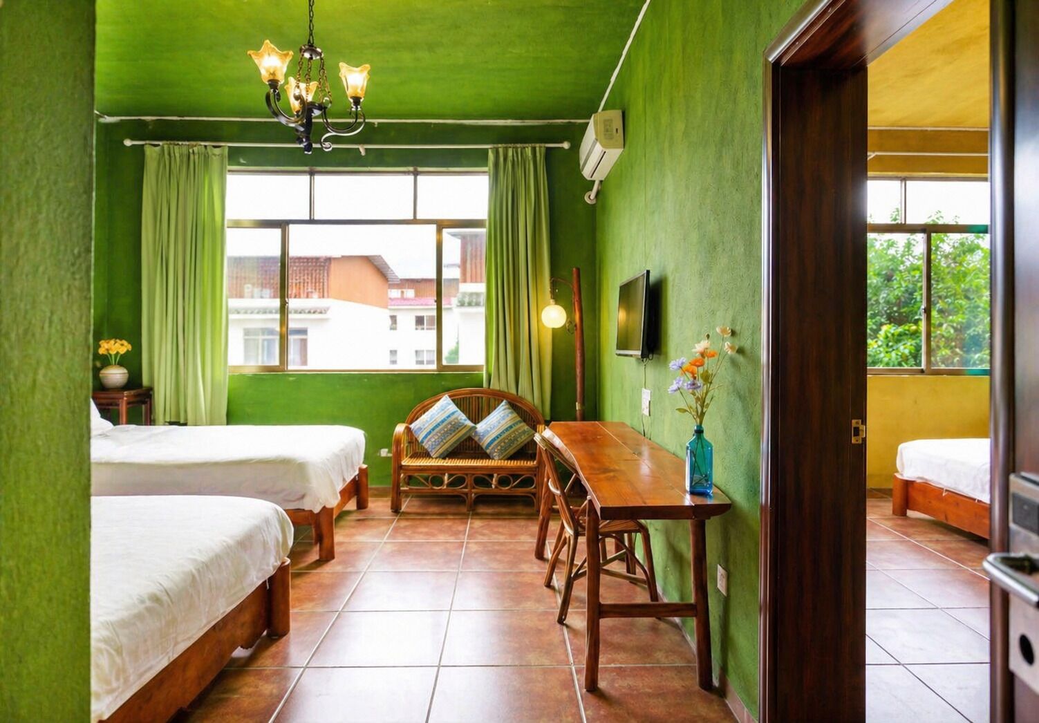 A room with two beds, a wooden dining table, a chandelier, a TV, and a window with a view of buildings.