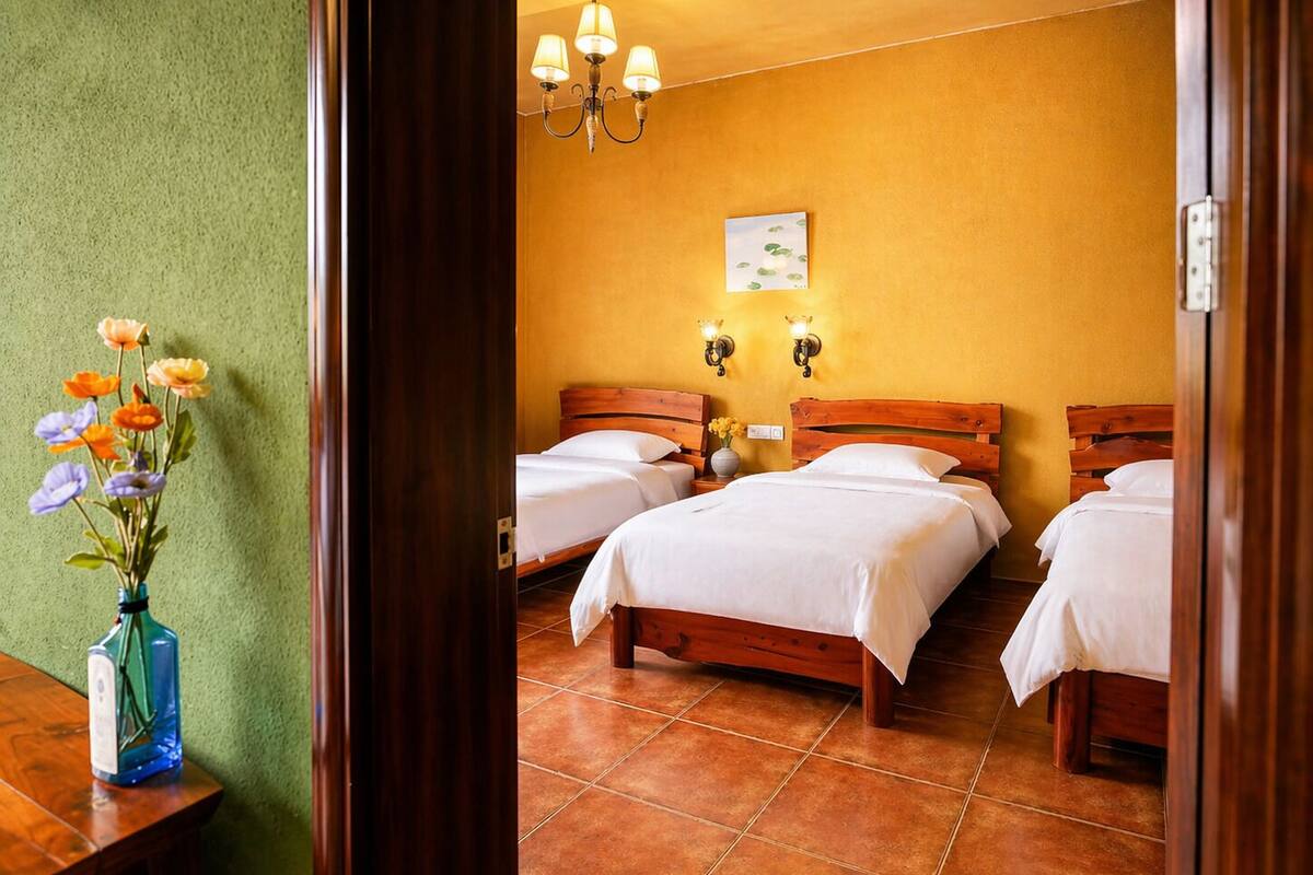 A hotel room with three wooden beds, a green wall, and a vase of flowers on a table.