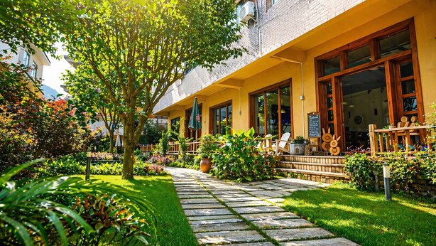 A building with a yellow facade, large windows, and a garden with a stone pathway. - Yangshuo Eden Inn (Guilin)
