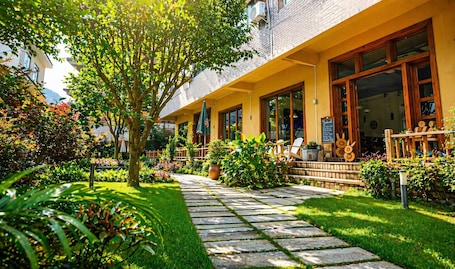 A building with a yellow facade, large windows, and a garden with a stone pathway.. Yangshuo Eden Inn