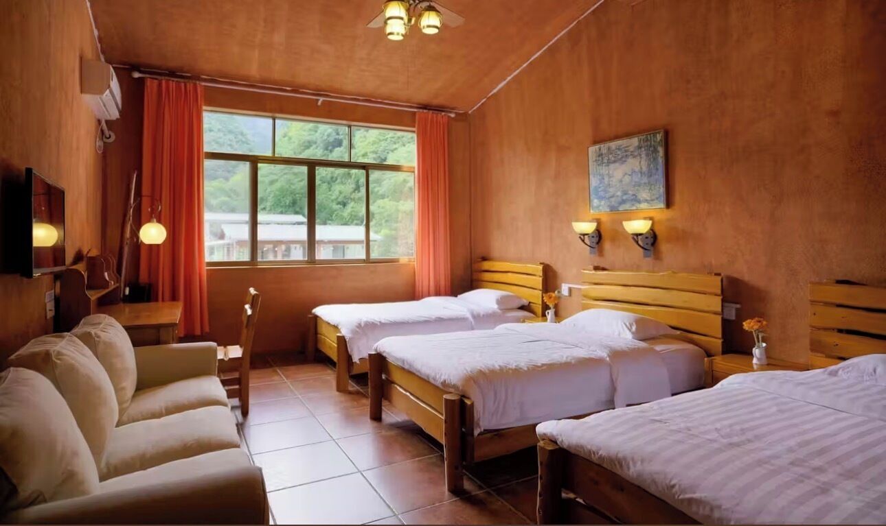 A hotel room with two beds, a sofa, a TV, and a window with curtains.