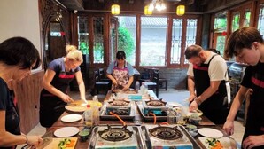 A group of people cooking in a traditional kitchen with wooden walls and large windows. - Yangshuo Eden Inn (Guilin)