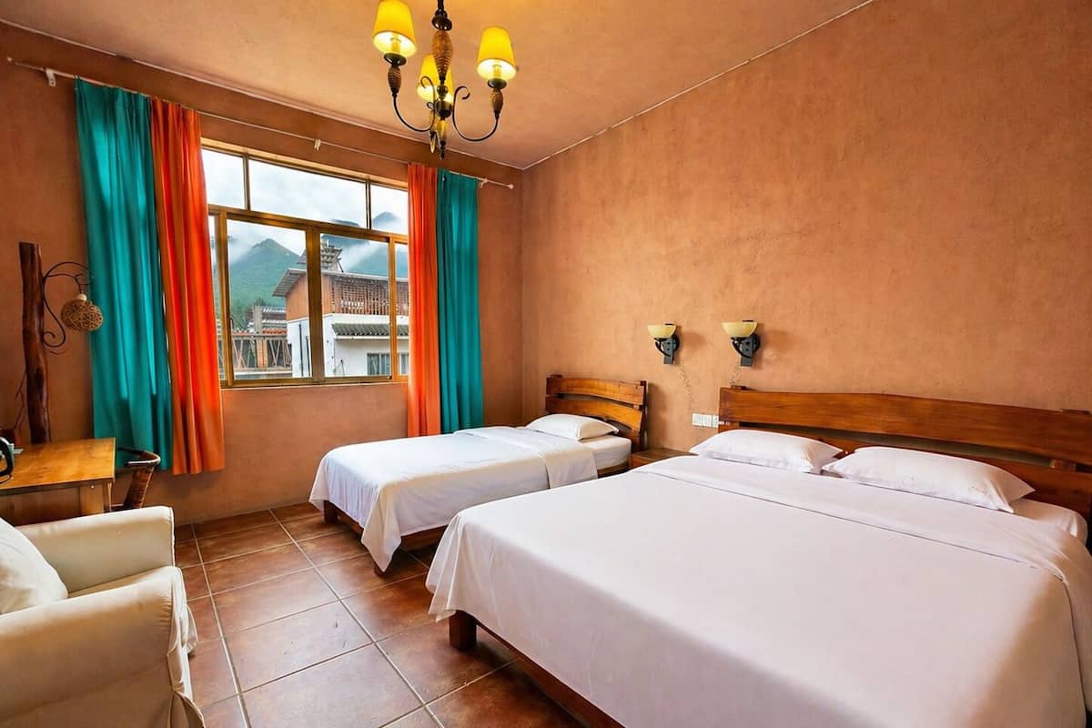 A hotel room with two beds, a wooden headboard, a desk with a chair, a window with curtains, and a chandelier.