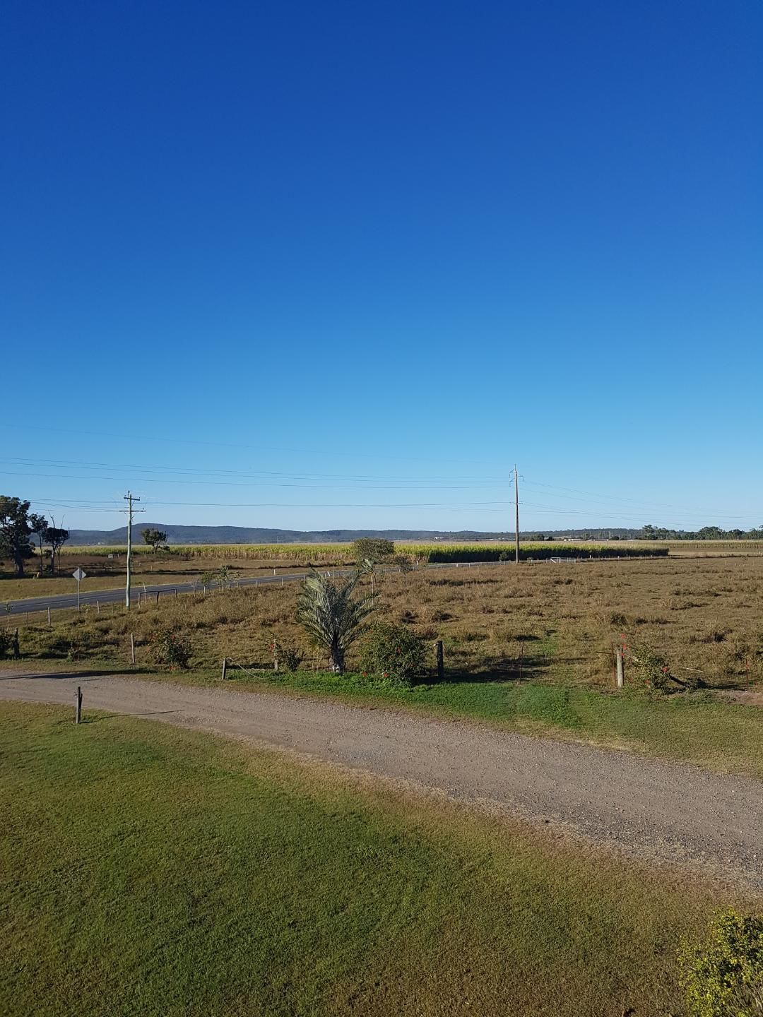 Paisagem rural com estrada de terra, campos e colinas ao longe.