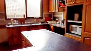 A kitchen with wooden cabinets, a stainless steel countertop, a microwave, and a window. - St Kilda East backpackers' hostel (St. Kilda East)