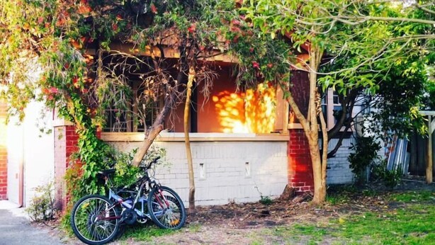 A bicycle parked under a tree in front of a building with a brick wall and a window. - St Kilda East backpackers' hostel (St. Kilda East)