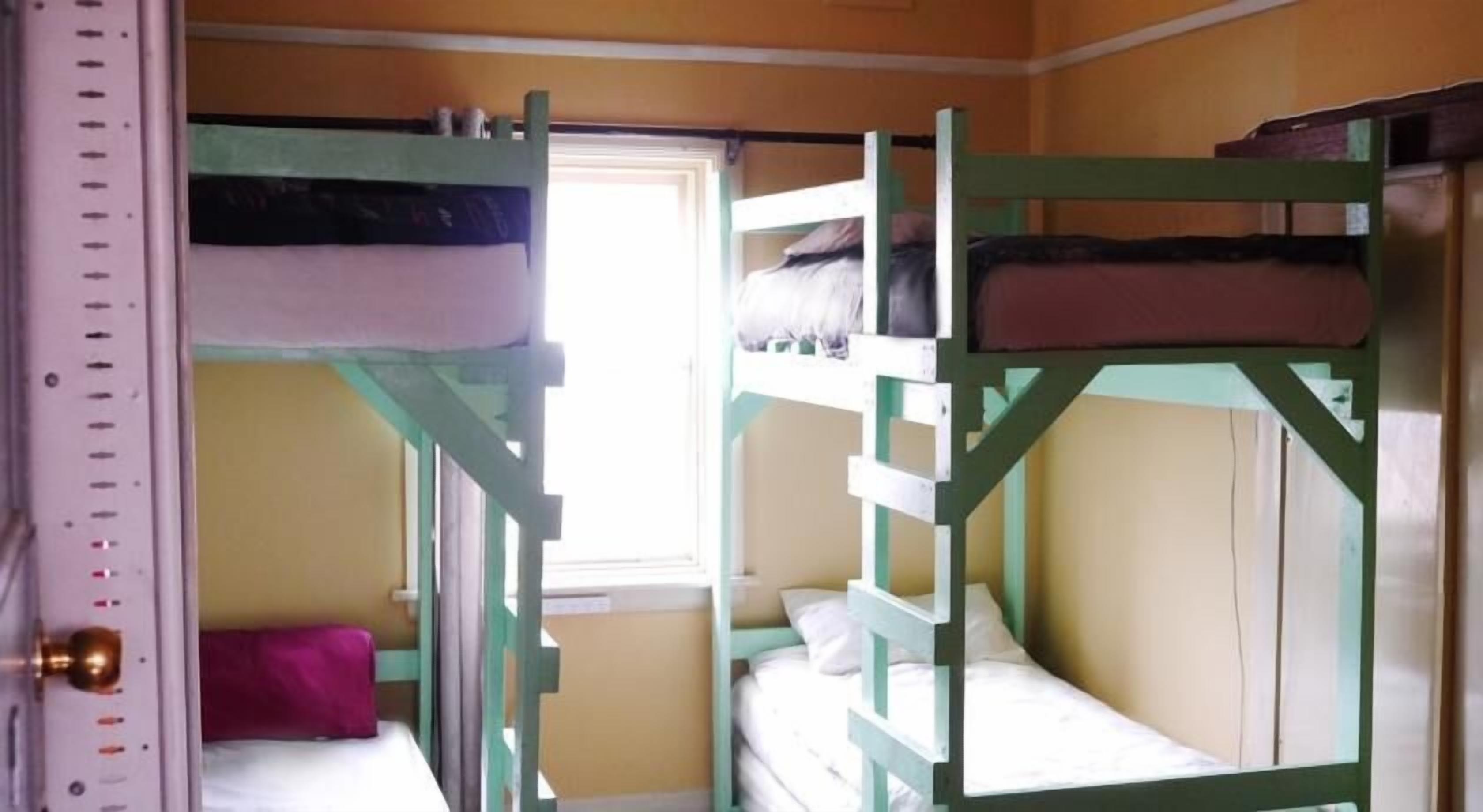 Une chambre avec un lit superposé, une fenêtre, une porte et un oreiller rose.