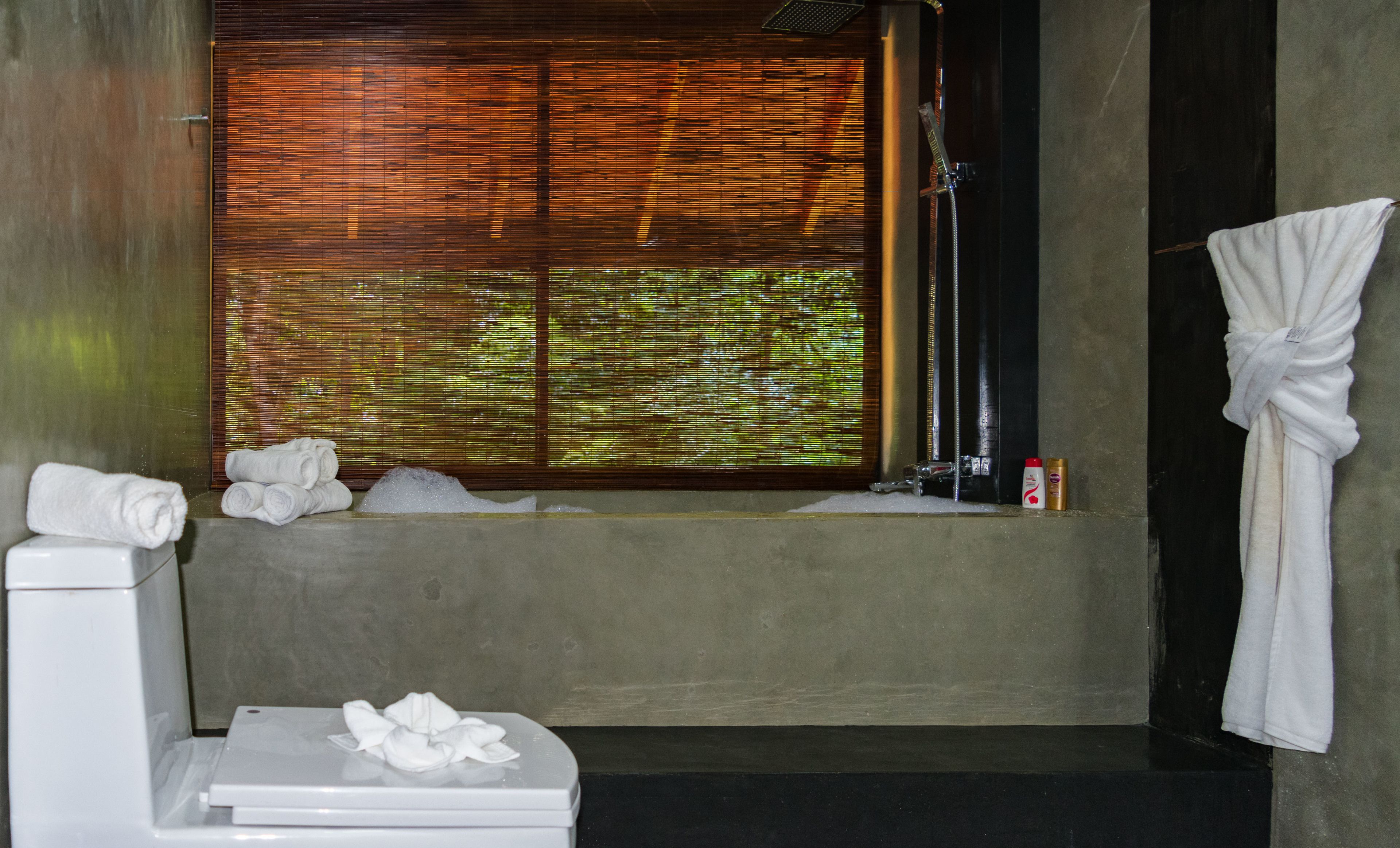 Ein Badezimmer mit Toilette, einem Fenster mit Jalousien, einer Dusche und einem Handtuchhalter.
