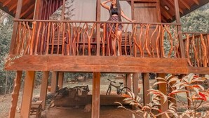 A wooden cabin with a balcony, a bicycle, and a rustic interior. - Kandy Cabana Eco Resort (Weligalla)