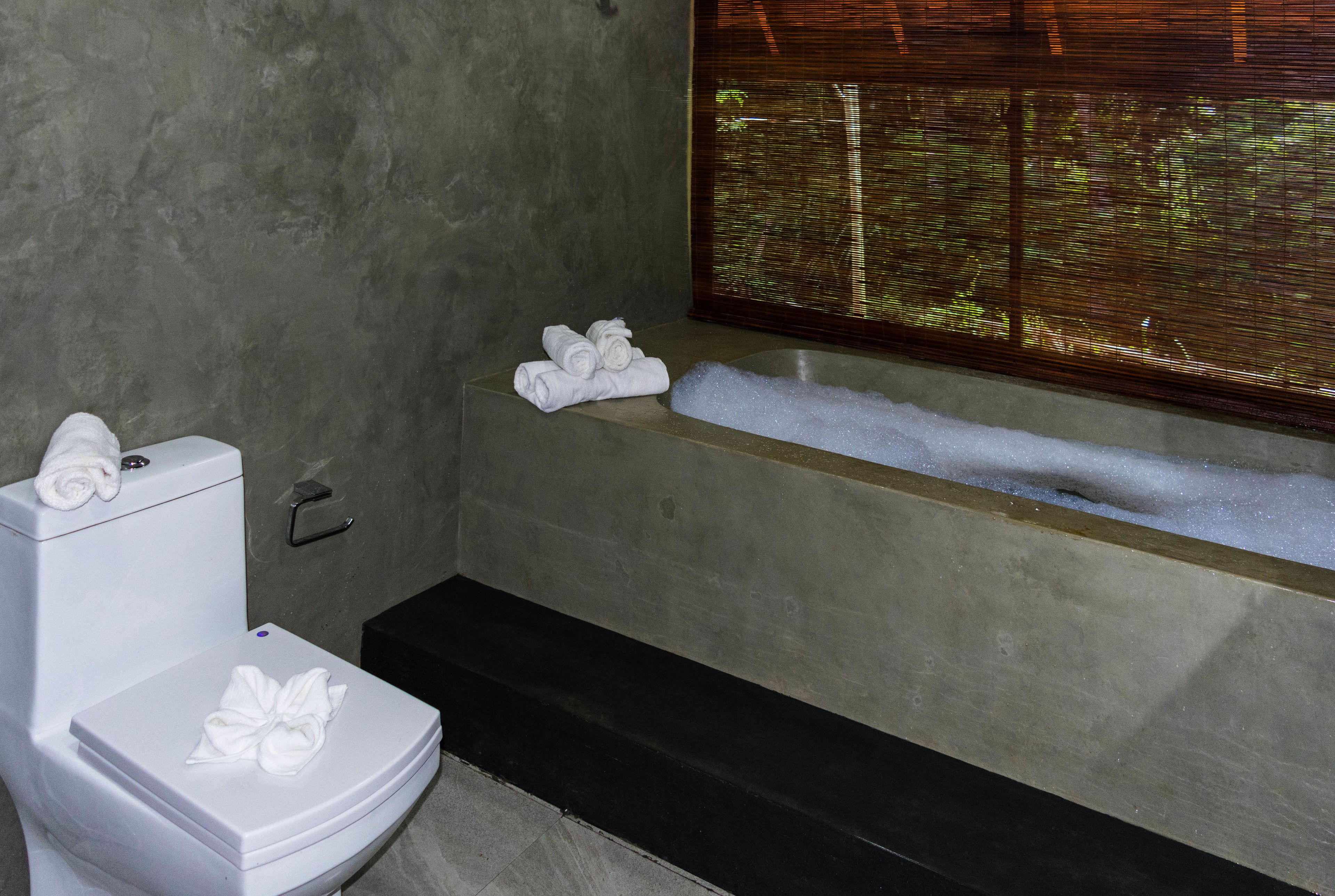 Un baño con inodoro, bañera y ventana con persianas.