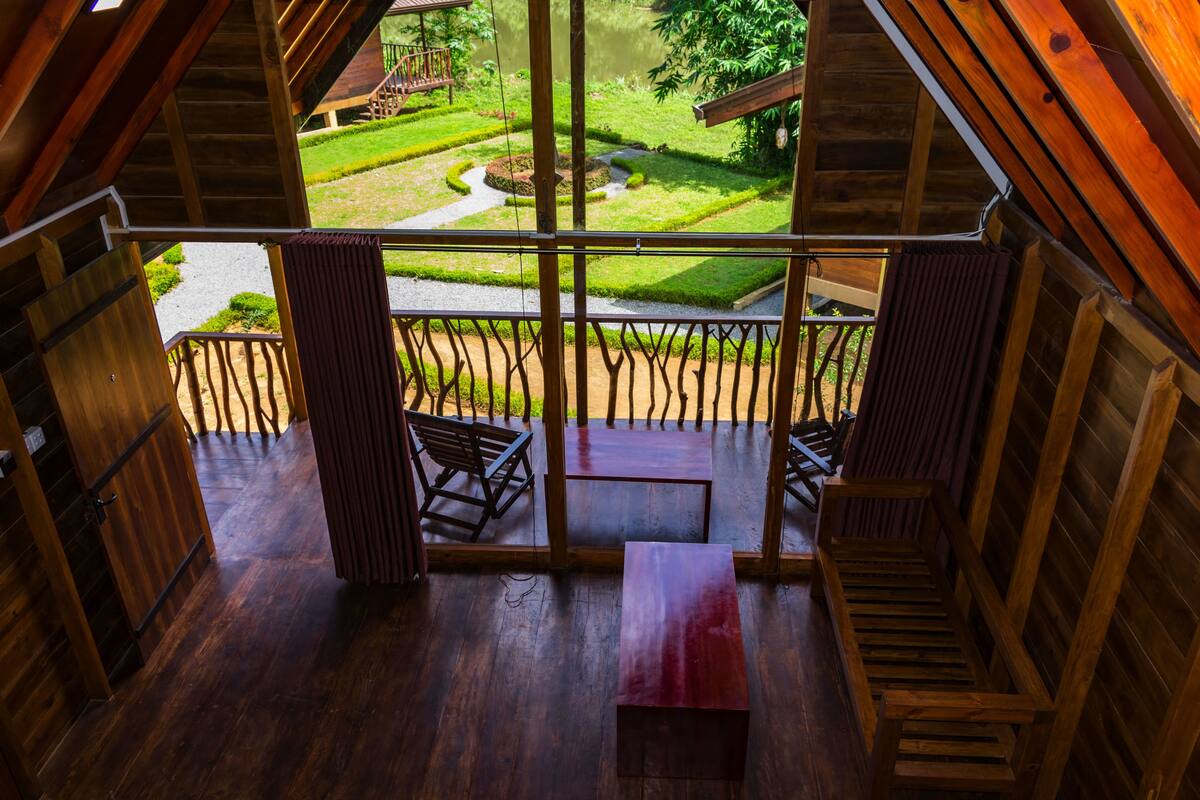 Un balcón de madera con vistas a un jardín cuidado y un sendero.