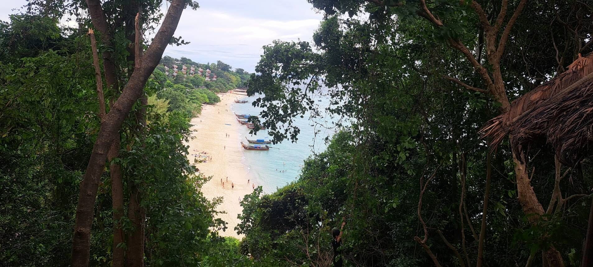 Une plage avec des bateaux et des gens, entourée d’une végétation luxuriante.