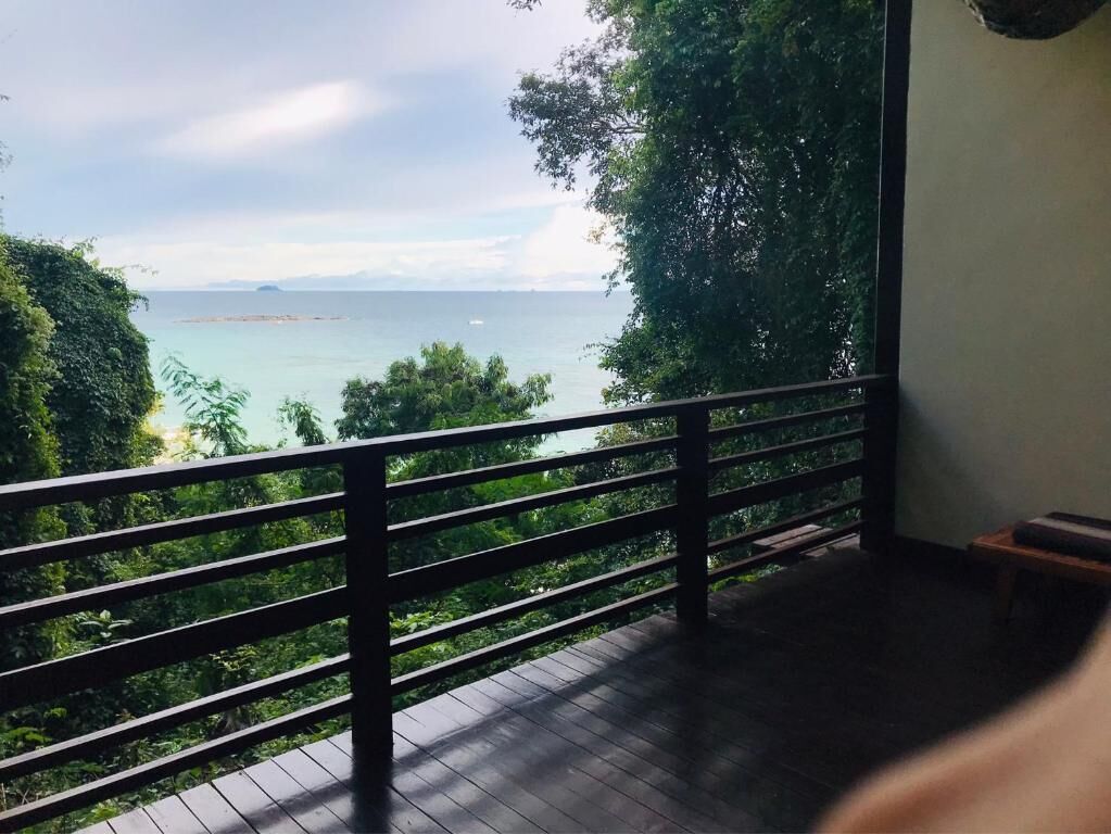 A balcony with a view of the sea and surrounding greenery.