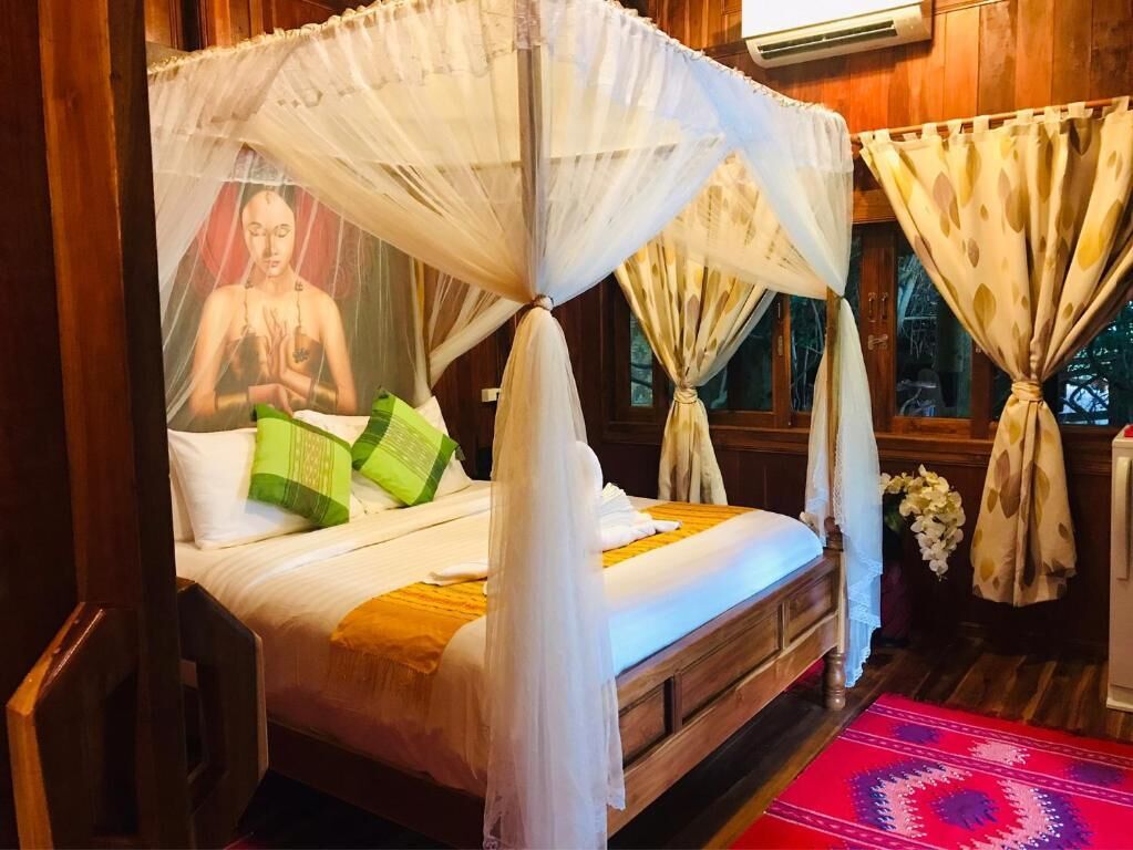 A bed with a canopy, pillows, a red patterned rug, and curtains.