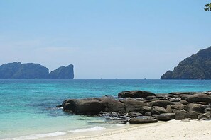 A beach with clear turquoise water, large rocks in the foreground, and distant mountains. - Viking Nature Resort (Ko Phi Phi)