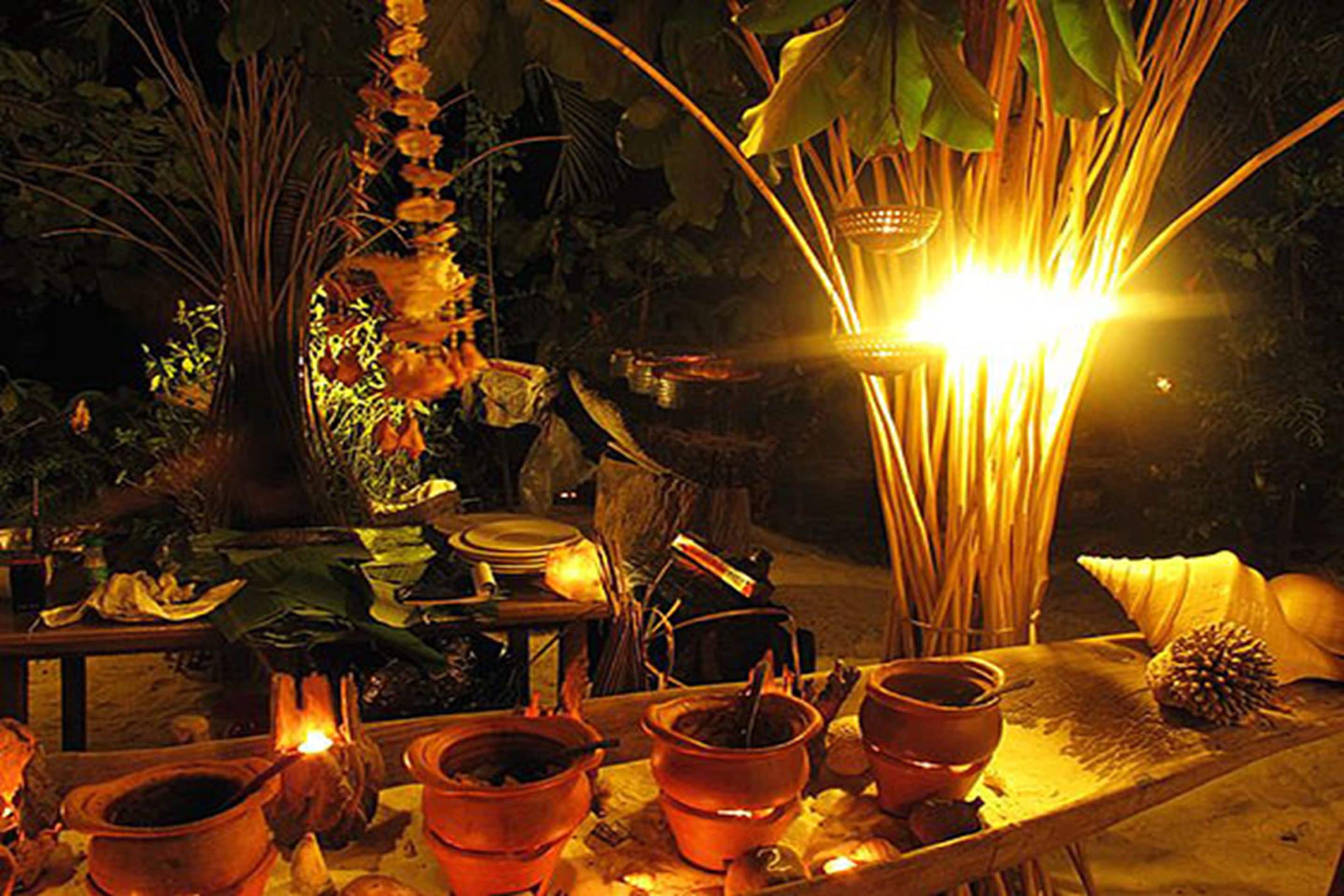 A rustic outdoor setting with a table displaying various items such as pots, a lantern, and a hanging plant.