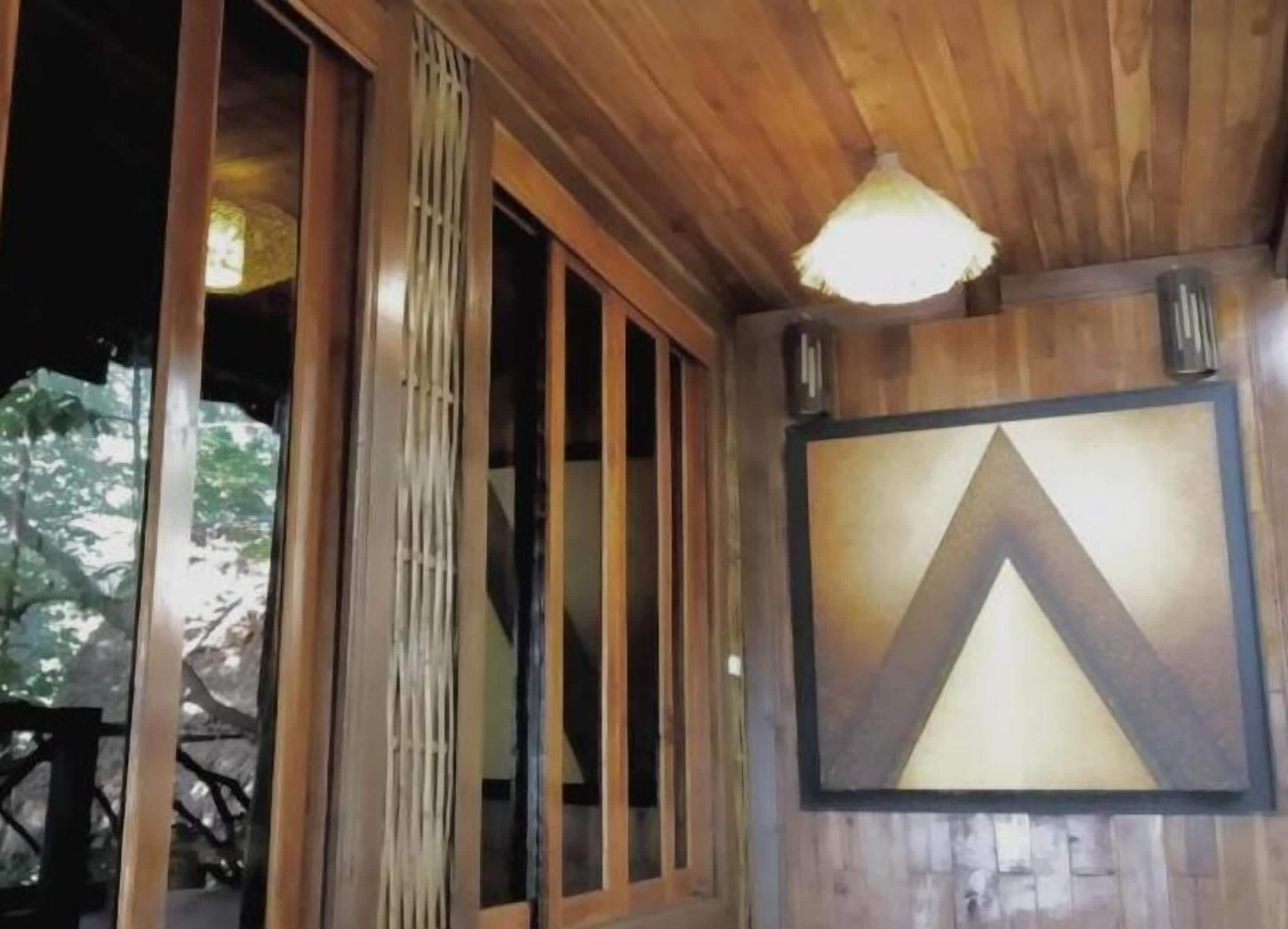 A wooden interior with large windows, a hanging light fixture, and a geometric wall decoration.
