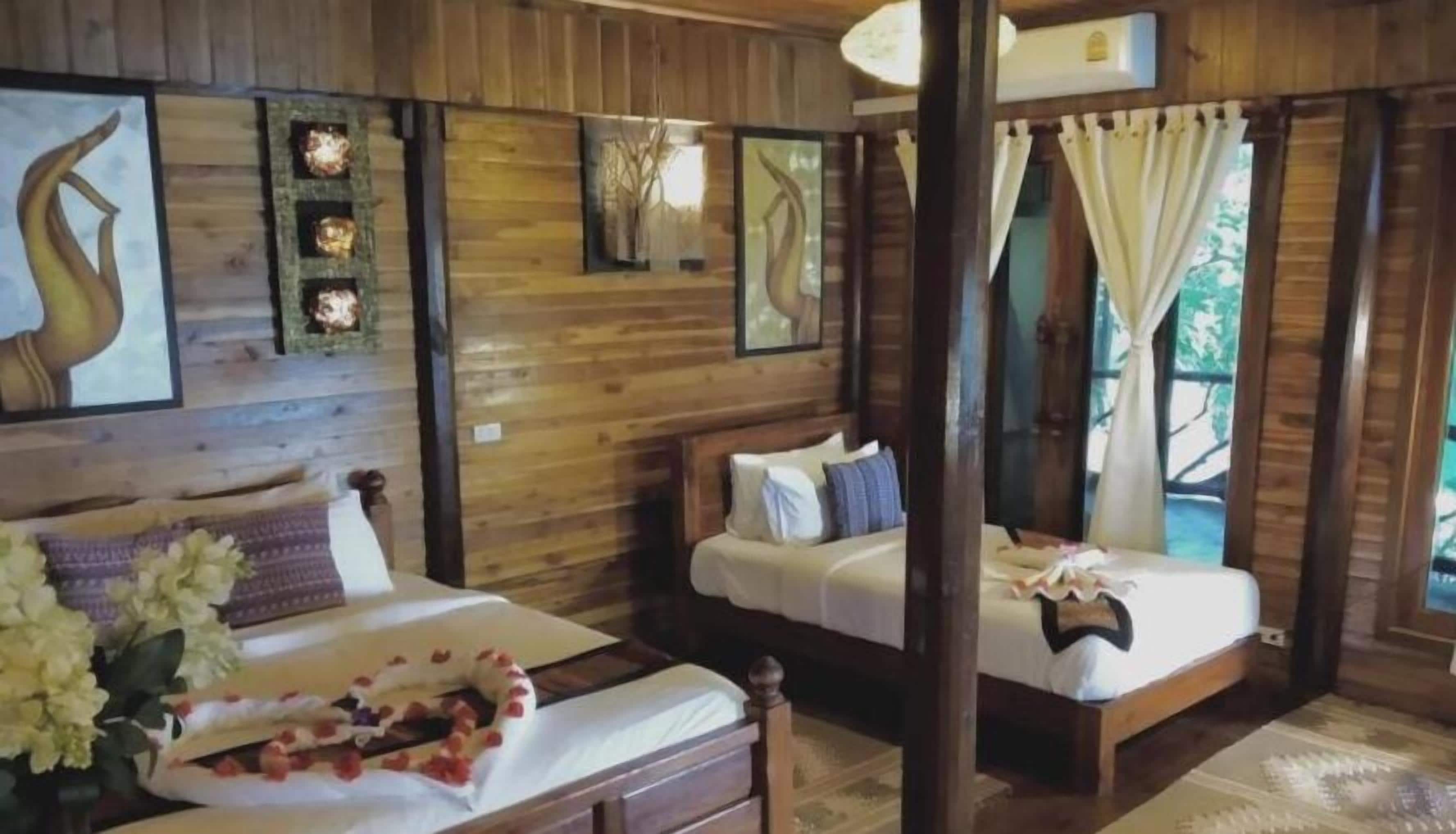 Ein holzgetäfeltes Zimmer im Blockhausstil mit zwei Betten, einem großen Fenster mit Vorhängen und Wandleuchten.