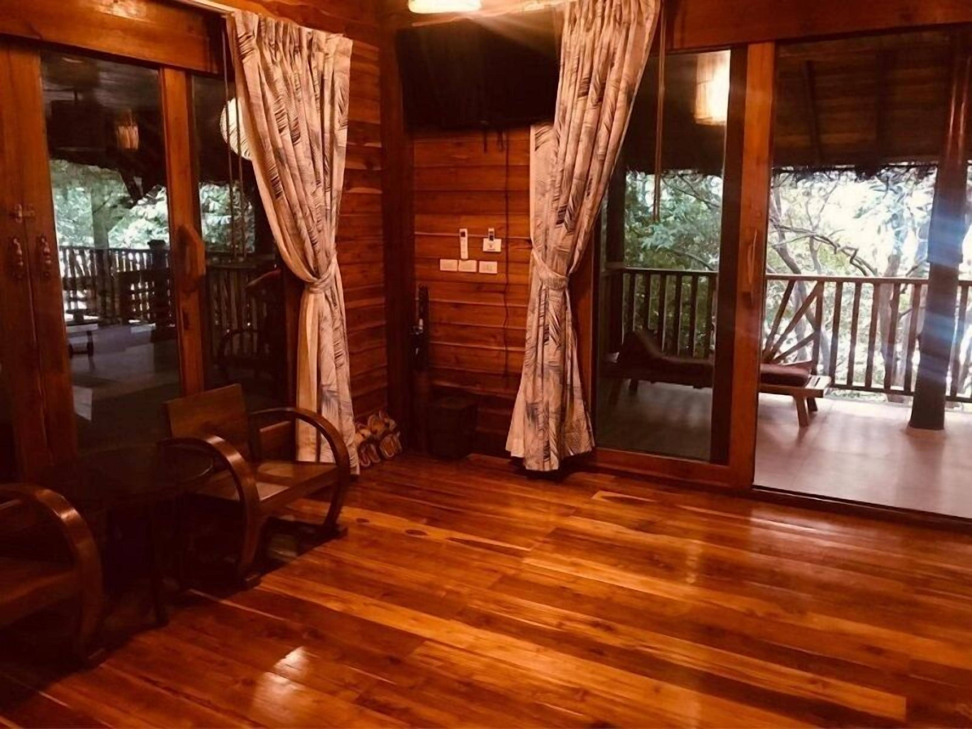 A wooden cabin interior with a wooden floor, a wooden chair, and a large sliding glass door leading to an outdoor deck.